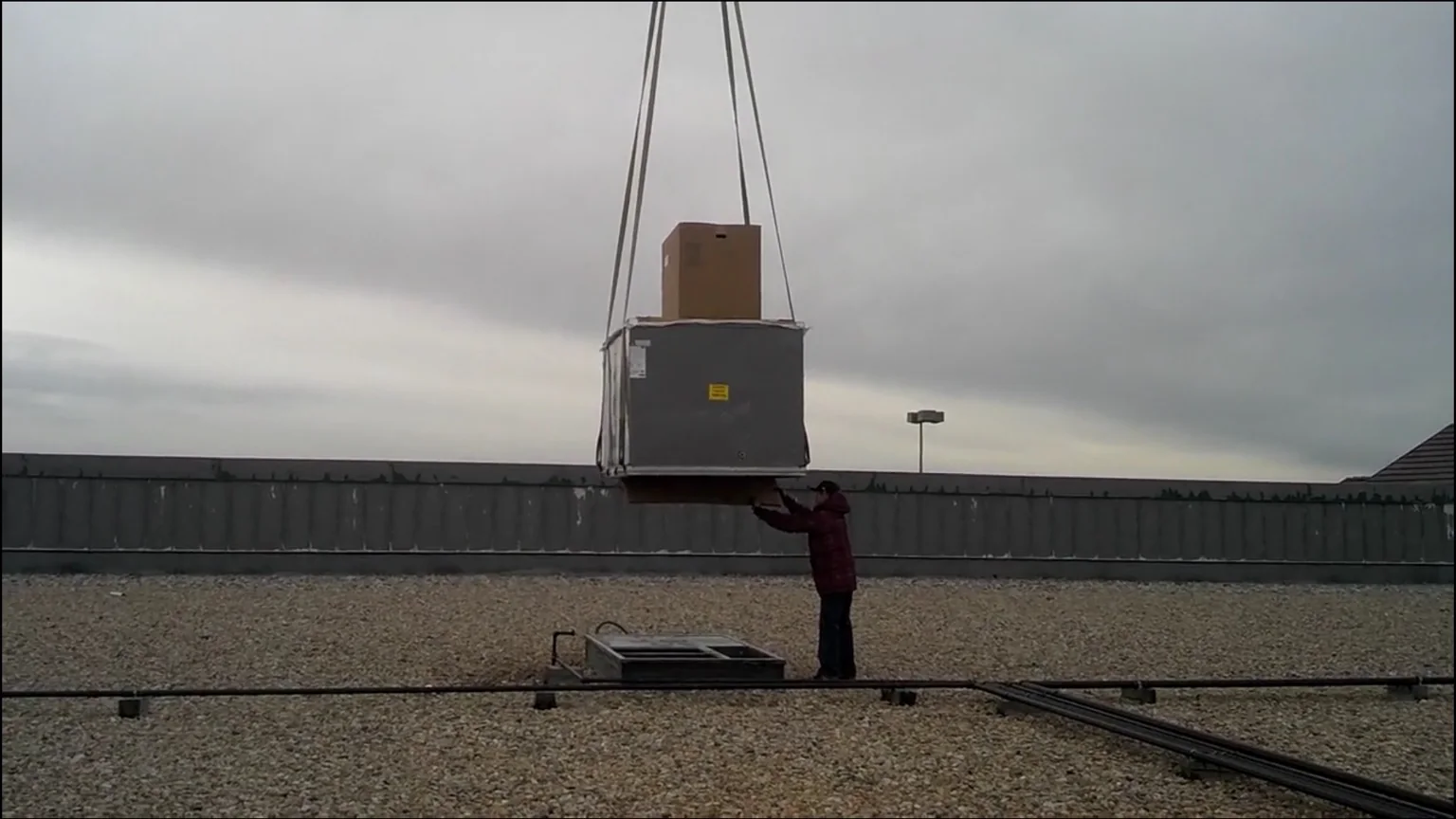 Commercial rooftop HVAC unit being positioned by crane